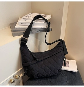 Detailed shot of a black quilted crescent crossbody bag with adjustable strap on a chair
