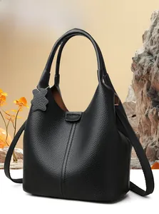 Dettaglio di borsa tote in pelle nera con manici sottili e ciondolo a forma di orsetto
