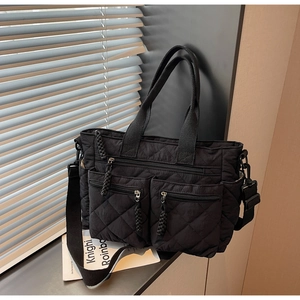 Detail of black quilted nylon tote bag featuring dual front zipper pockets and top handles