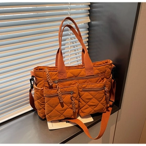 Detail view of orange quilted tote bag showing multi-pocket system and woven zipper puller