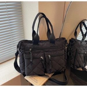 Macro view of black quilted nylon tote bag featuring front dual zipper pockets and top handles