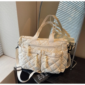 Detail of white quilted tote bag with multiple zipper pockets and adjustable strap