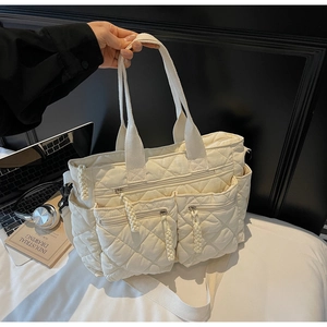 Detail of off-white quilted tote bag showing three functional front zipper pockets