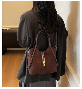 Close-up of a vintage dark brown suede tote bag with a golden metal buckle and long strap
