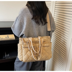 Detail of a beige quilted tote bag with multiple zip pockets and a wide strap
