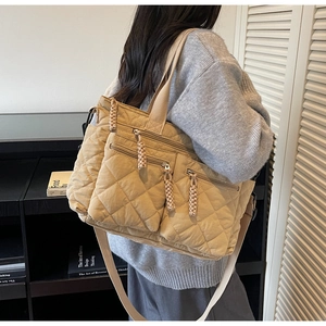 Detail of khaki quilted tote bag featuring multiple front zip pockets and woven pullers