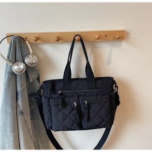 Detail of black quilted nylon tote bag with utility zippers on a minimalist hanger