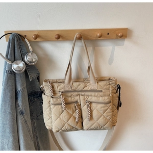 Detail of a beige quilted tote bag featuring multiple zippered pockets on wooden wall hook