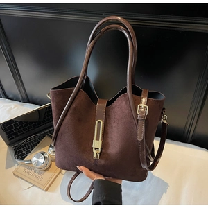 Detail of dark brown suede tote bag featuring a gold metal buckle on white desktop