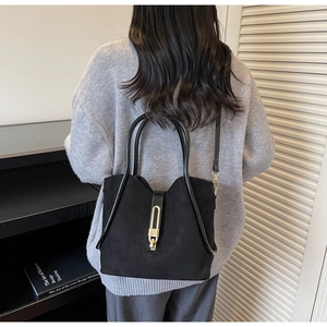 Detail of black suede bucket bag with gold metal buckle shown on model in minimal interior