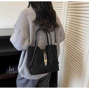 Detail of matte black bucket bag featuring glossy leather handles and gold metal buckle