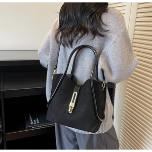 Detail of a black suede bucket bag featuring a sleek gold metal bar lock and round handle