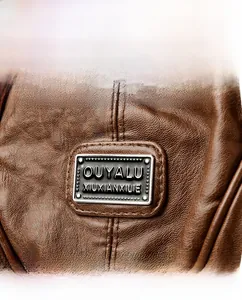Close-up of brown pebbled leather texture and rectangle silver logo plaque on the handbag