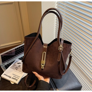 Detailed macro view of dark brown suede bucket bag with gold metal clasp on leather surface