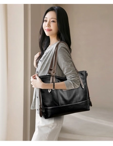 Detail view of black leather tote bag with brown straps and white contrast stitching