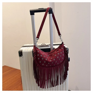 Détail du sac bandoulière bordeaux à franges et œillets sur une poignée de valise