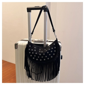 Détail du sac demi-lune noir à rivets et franges suspendu à une poignée de valise