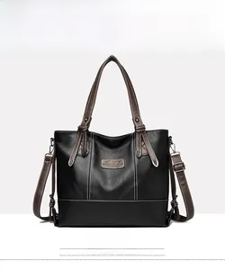 Front detail of black leather tote bag featuring brown handles and white contrast stitching