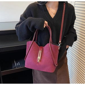 Detailed close-up of burgundy suede bucket bag with elegant gold metal buckle and strap