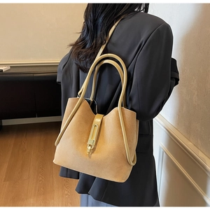 Detail of light brown suede tote bag with leather straps and gold buckle on shoulder