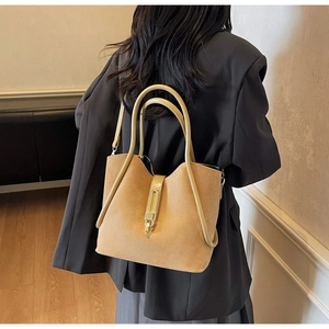 Detail of camel suede bucket bag featuring a unique arched handle and gold metal clasp
