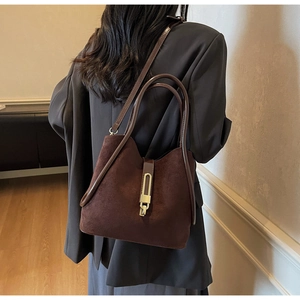 Close-up of dark brown suede bucket bag with gold metal clasp in a stylish indoor setting