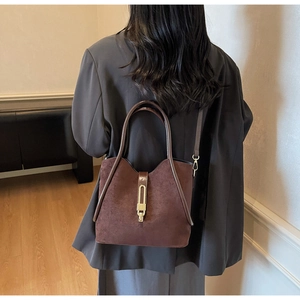 Detail of brown suede bucket bag with gold metal lock and leather handle shown on model