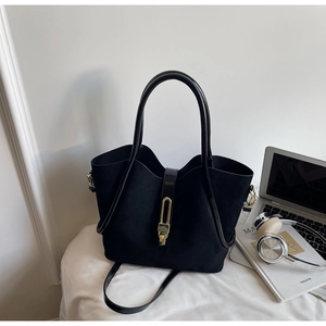 Detail of black matte tote bag featuring gold metal lock and leather handles in office setting
