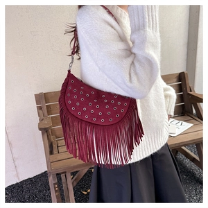 Détail d'un sac à franges bordeaux avec œillets argentés porté sur un pull en maille