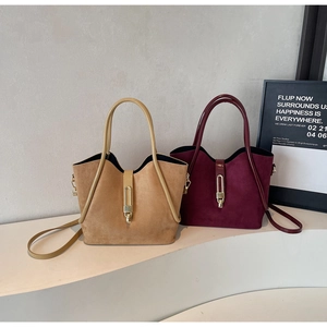 Detail of red and camel suede tote bags with golden metal buckles on a white platform