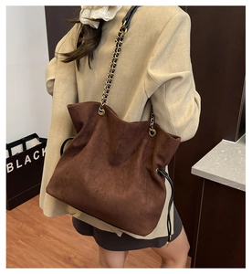 Detail of brown suede bucket bag featuring chain strap and drawstring closure for women