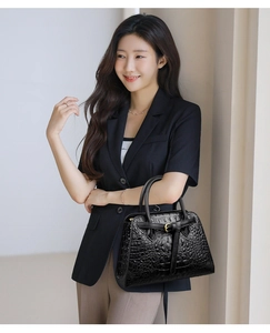 Close-up of black crocodile-embossed leather texture and gold buckle on handbag