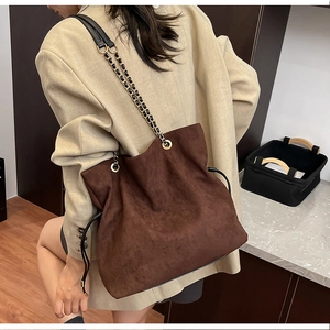 Detail of dark brown matte bucket bag with gold chain strap on a model shoulder