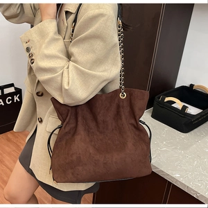Detail of dark brown suede bucket bag featuring golden chain strap and drawstring accents