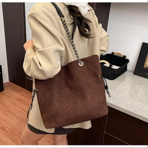 Close-up of brown suede drawstring bucket bag with gold chain and black leather strap