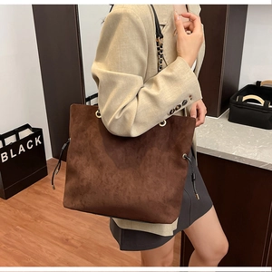 Detail of brown suede bucket bag featuring drawstring closure and gold metal chain strap