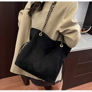 Close-up of matte black bucket bag with gold-tone chain straps and drawstring detail