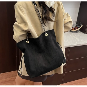 Detail of black suede bucket bag featuring drawstring and metal chain shoulder strap