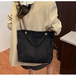 Detail of black suede drawstring bucket bag with gold chain strap on shoulder
