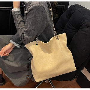 Detailed close-up of warm beige suede bucket bag with gold chain strap and drawstring tassels