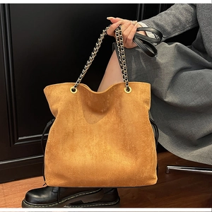 Detail of camel suede bucket bag with gold chain strap and drawstring on model