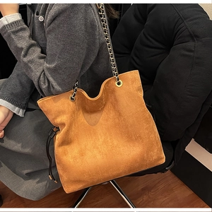Detail of a brown suede bucket bag with chain strap and drawstring closure on model