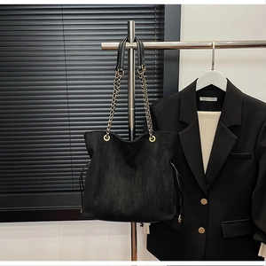 Close-up of black suede bucket bag with gold chain strap and drawstring detail