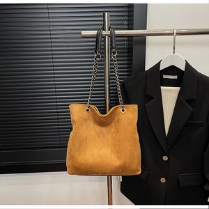 Detail of camel suede bucket bag with gold chain strap and black leather shoulder handle