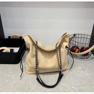 Detail of beige suede bucket bag featuring drawstring closure and black gold chain strap