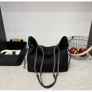 Detail of black faux suede bucket bag featuring drawstring and chain shoulder strap