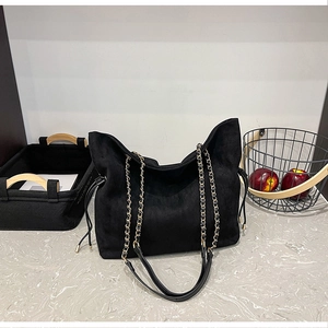 Close-up of black suede bucket bag featuring gold chain strap and drawstring detail