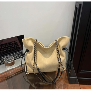 Close-up of beige suede bucket bag with gold chain strap and drawstring detail