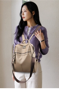 Dettaglio zaino in pelle beige con cerniere argentate e tracolla in tessuto larga