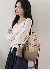 Dettaglio zaino in pelle beige con cerniere multiple e decorazioni con occhielli metallici